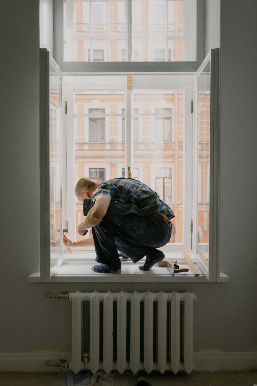Artisan agenouillé sur l'appui d'une fenêtre ouverte pendant la pose